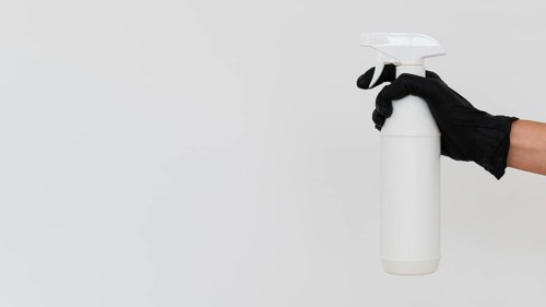 Hand with glove holding disinfectant bottle with copy space