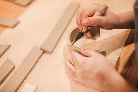Female potter s hand engraving clay with tools wooden table