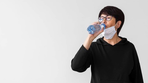 Woman with medical mask drinking water from bottle
