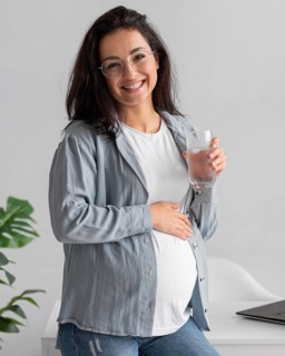 Smiley pregnant woman home holding glass water