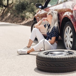 Sad young woman sitting near broken down car road