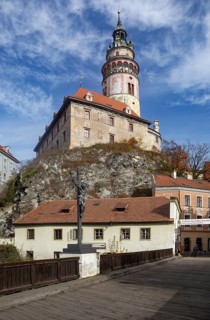 Pedestrian bridge over the Vltava with wayside cross and Krumlov Castle with castle tower