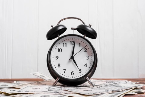 Alarm clock us dollar currency notes wooden desk against white wall