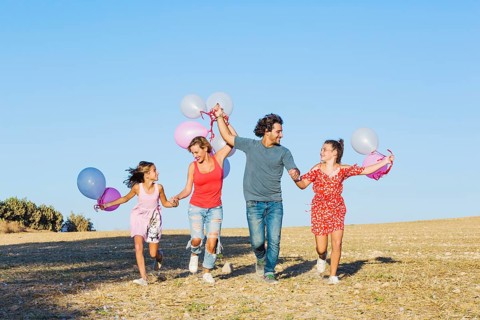Family running field holding balloons