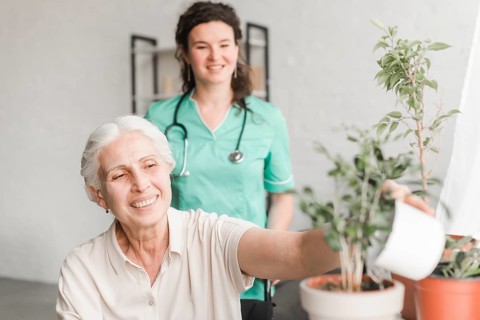 Nurse looking senior woman sitting wheelchair watering plant