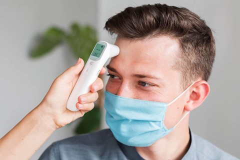 Man with medical mask checking temperature office with thermometer
