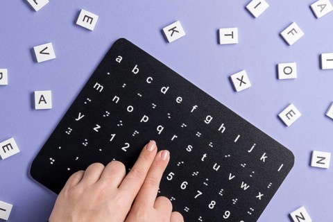 Fingers touching braille alphabet board