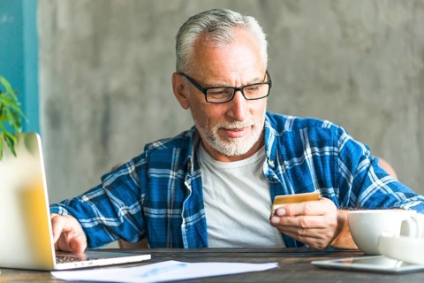 Senior man reading credit card number while working laptop