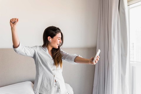 Smiling portrait young woman holding mobile phone hand dancing