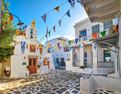 Beautiful morning view of small square decorated for some celebrations with flags in typical Greek town. Greek Orthodox church