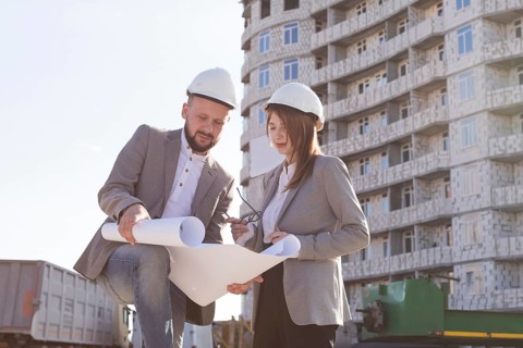 Two architects holding blueprint discussing project while working together