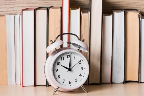White alarm clock showing 10 o clock front bookshelf wooden desk