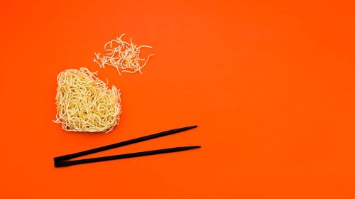 Broken dry instant noodles with chopsticks orange background