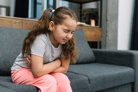 Little girl holding hands her stomach suffering from pain