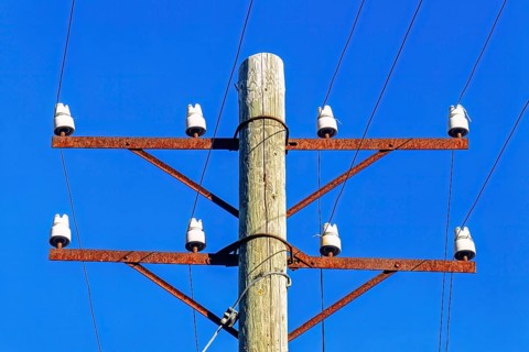 Old telephone pole with porcelain insulators and telephone wire at a blue sky