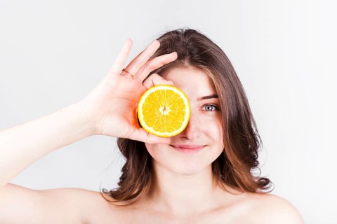 Smiling woman holding orange slice face