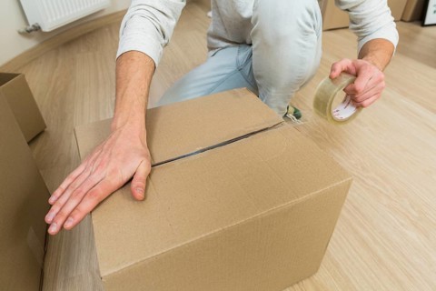 Close up male sealing cardboard box with adhesive tape