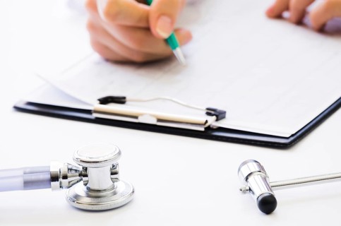 Close up doctor s hand holding pen checking medical report clipboard