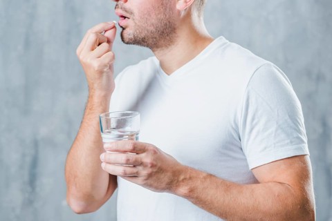 Young man holding glass water taking medicine