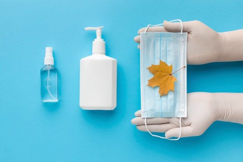 Top view hands holding medical mask with autumn leaf liquid soap bottle