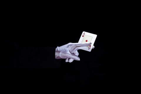 Magician holding aces playing card fingers against black background