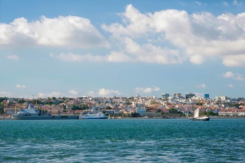 View of Tagus river with tourist boat and moored NATO warships in Lisbon
