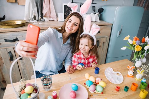 Young woman taking selfie with daughter near easter eggs