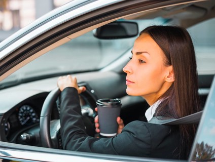 Young businesswoman holding disposable coffee cup driving car