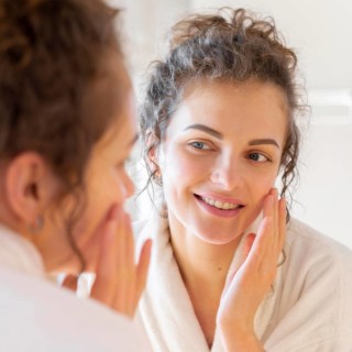 Woman applying cream face while looking mirror