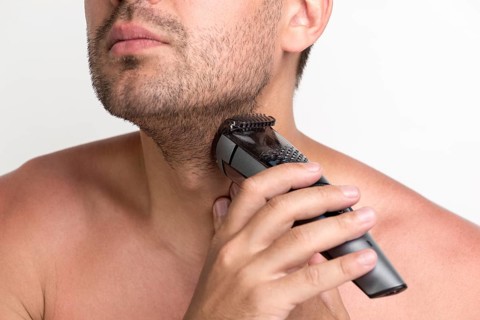 Portrait young man shaving his beard with electric shaver