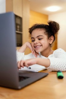 Happy little girl home during online school with laptop