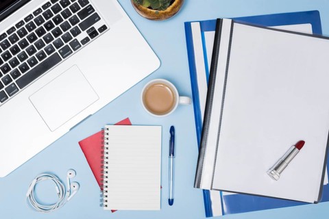 High angle view laptop folders coffee cup earphone spiral notepad pen against blue background