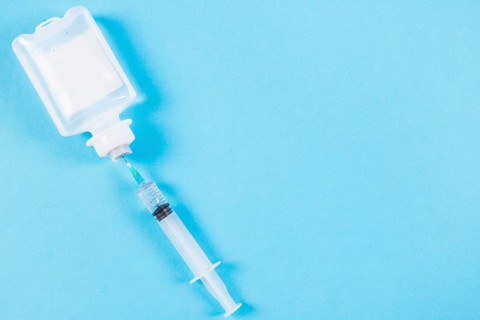 Syringe inserted normal saline solution plastic bottle blue background