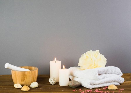 Illuminated candles towel spa stones loofah mortar pestle wooden surface