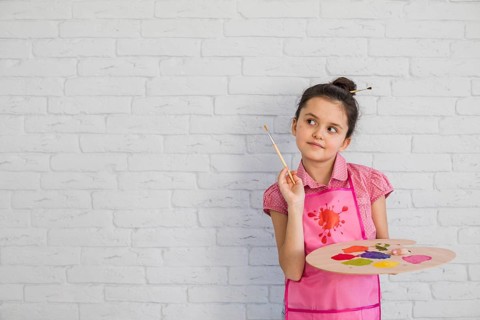 Portrait girl with paintbrush palette standing against white wall
