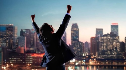 Excited businessman celebrates with his fists in the air with the city in the background