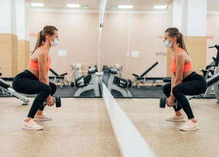 Woman gym training with medical mask front mirror