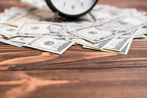 Close up alarm clock us dollar currency notes wooden desk