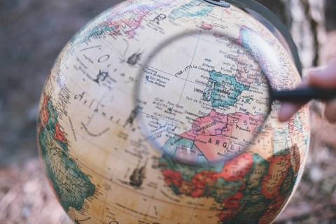 Person with magnifying glass looking globe