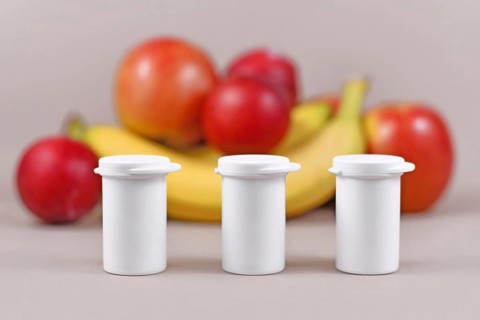 Small bottles with food nutrition supplements in front of fruits and vegetables in blurry blue background