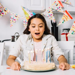 Surprised birthday girl blowing cake with illuminated candles