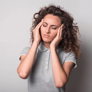 Woman with closed eyes having headache against gray background