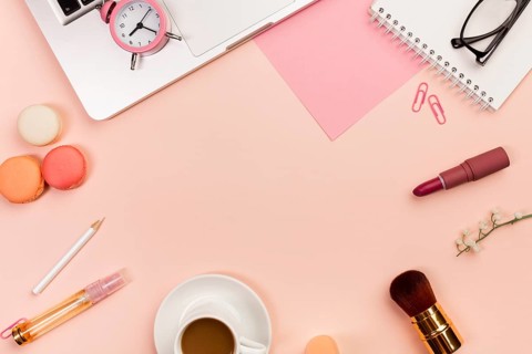 Macaroons coffee cup makeup brushes alarm clock laptop peach colored background