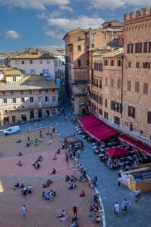 Tourists rest on the Piazza del Campo or sit in street cafes under red awnings