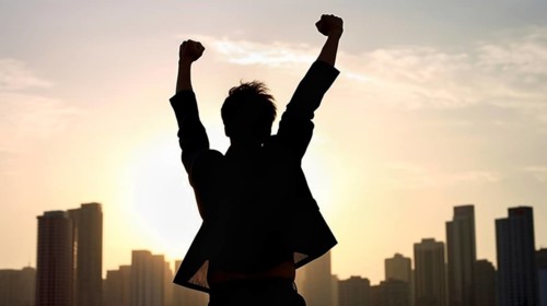 Excited businessman celebrates with his fists in the air with the city in the background
