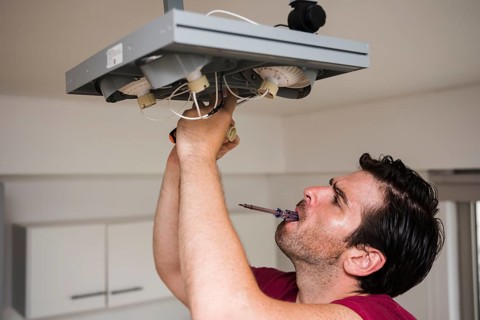 Man carrying tester mouth while repairing ceiling focus light home