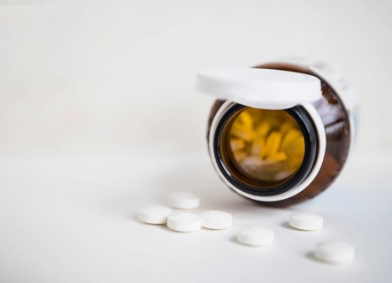 White round pills spilling from brown bottle white background