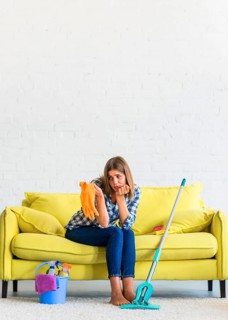 Sad young woman sitting yellow sofa looking orange rubber gloves