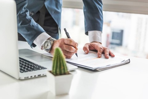 Businessman writing document with pen desk with laptop