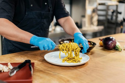 Male chef with gloves putting pasta plate
